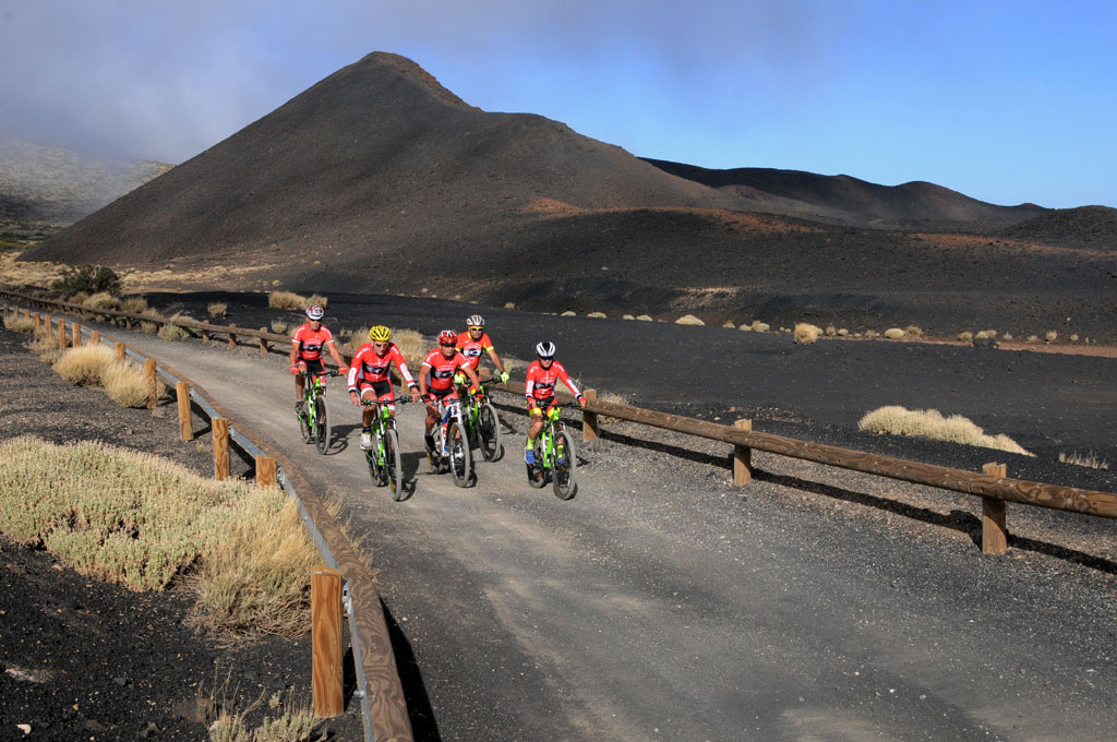 Ciclistas en un camino de tierra, paisaje volcánico en Tenerife al fondo.