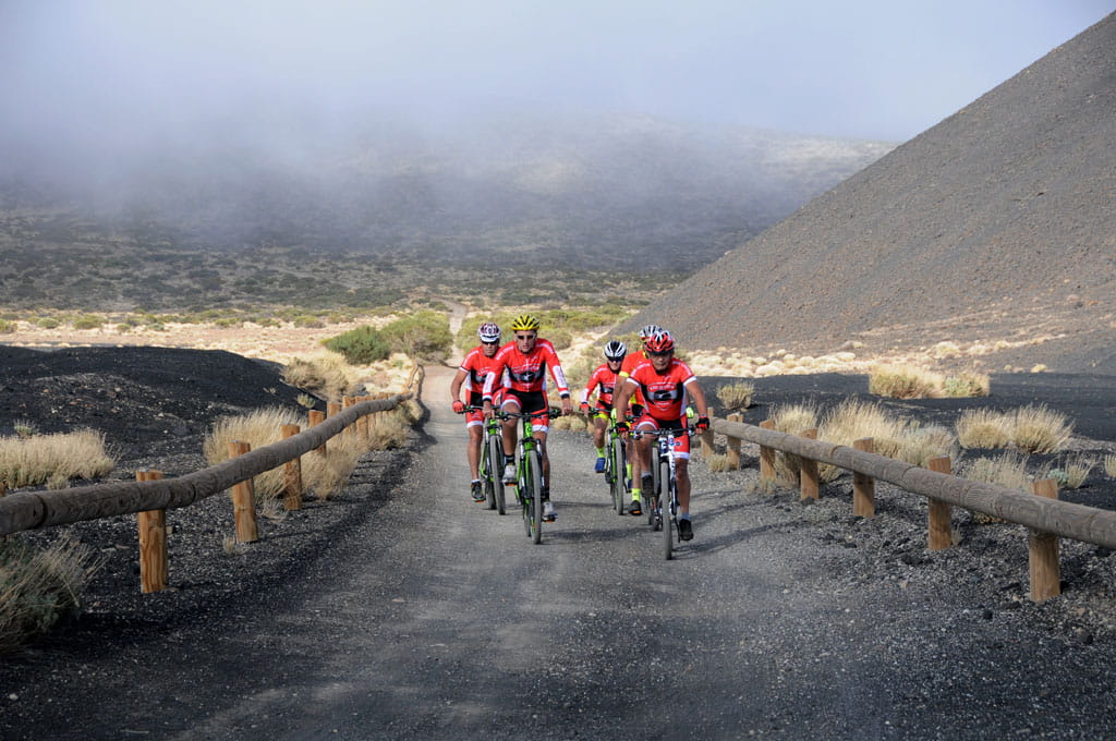 Ciclistas recorren sendero volcánico en Tenerife bajo cielo nublado.