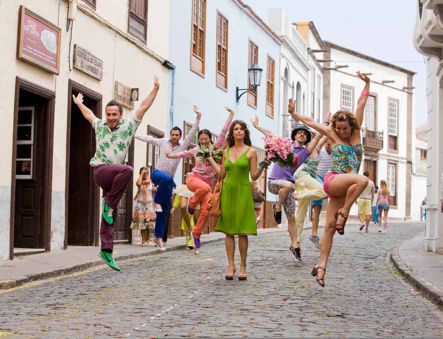 Personas bailando en una calle de La Laguna, Tenerife, con flores y ropa colorida.