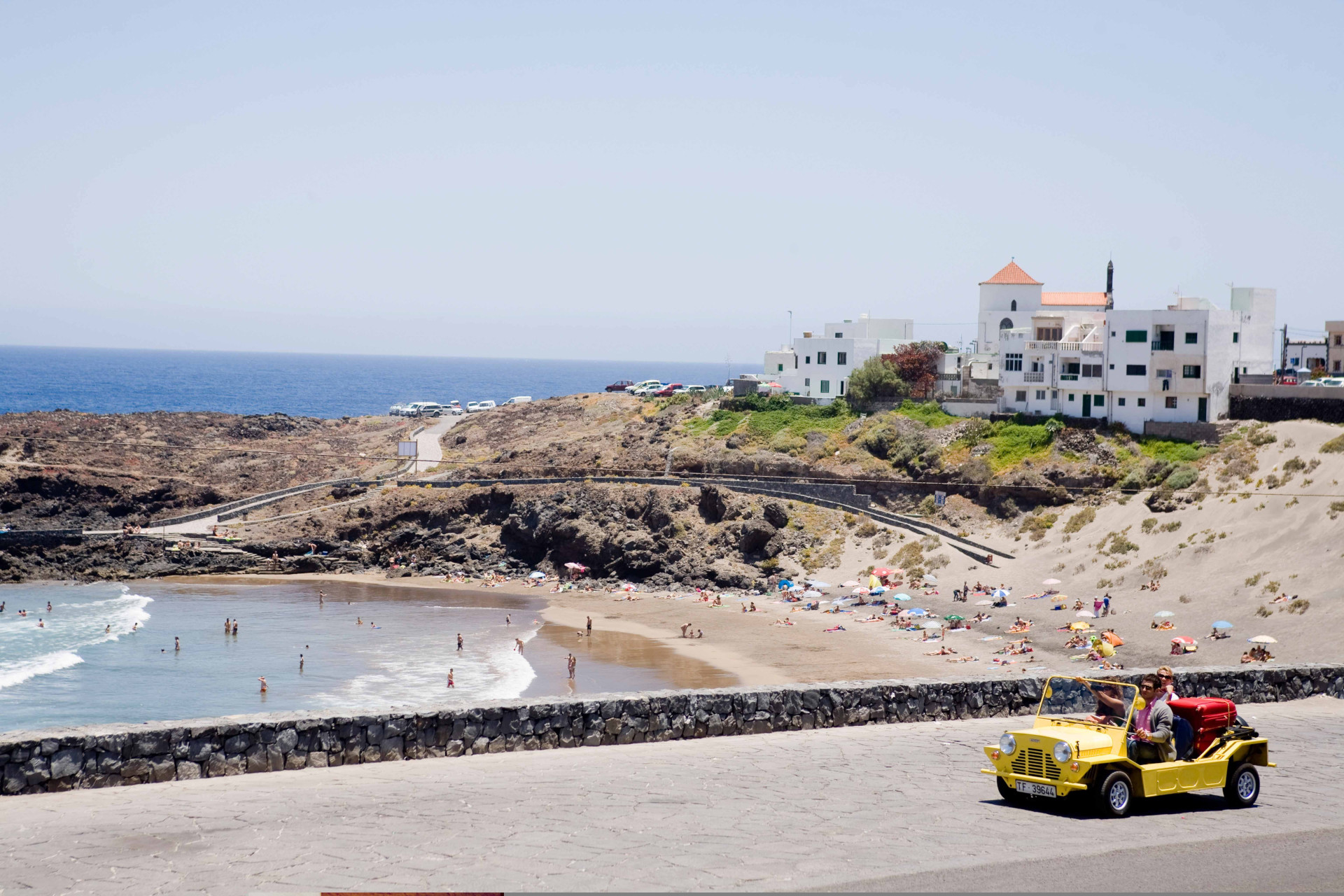 Playa de piscinas naturales con turistas y coche amarillo en La Punta, Tenerife.
