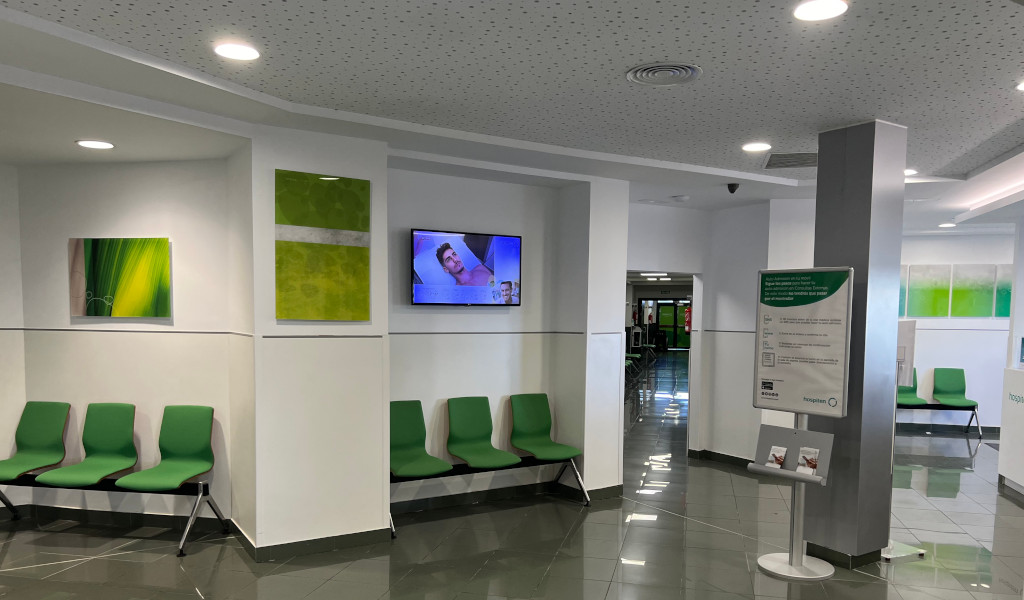 Sala de espera con sillas verdes y pantallas encendidas en clínica de Tenerife.