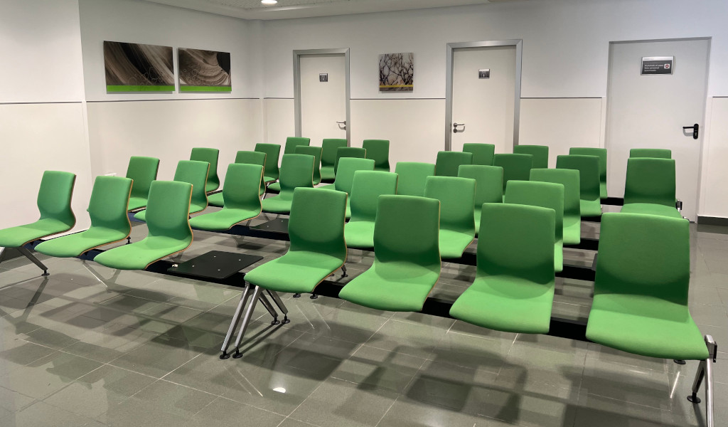Sala de espera con sillas verdes en Tenerife. Puertas y cuadros en la pared.