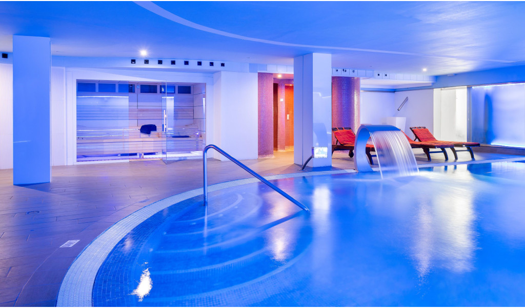 Piscina interior con cascada y tumbonas en spa de Tenerife.