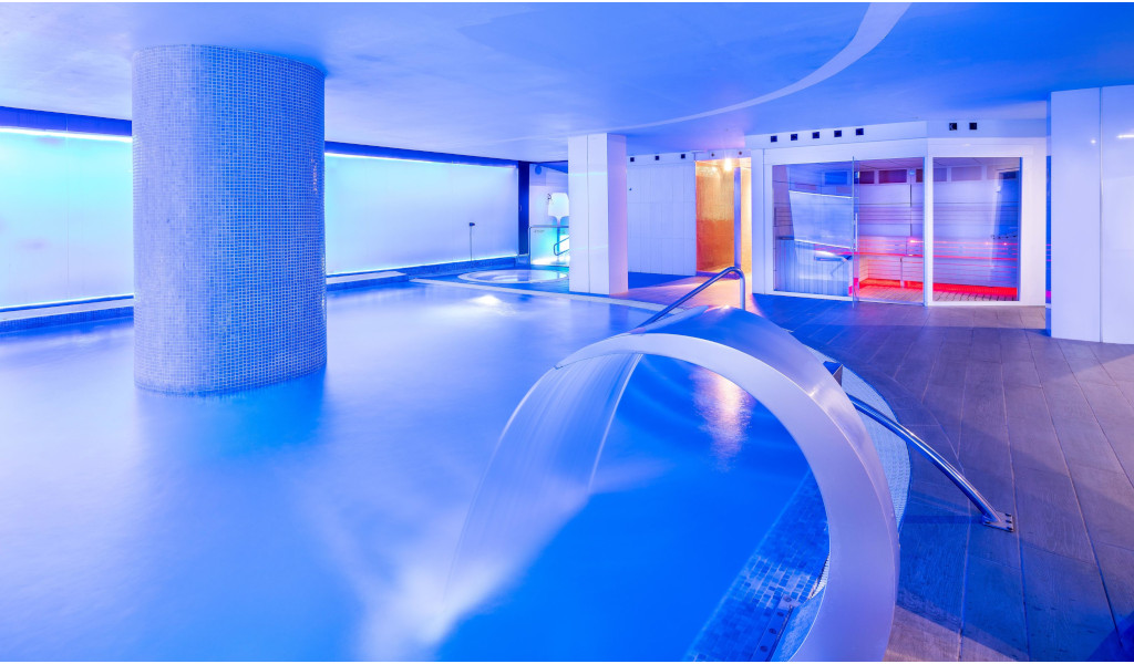 Piscina interior iluminada en hotel de Tenerife con chorro de agua y decoración moderna.