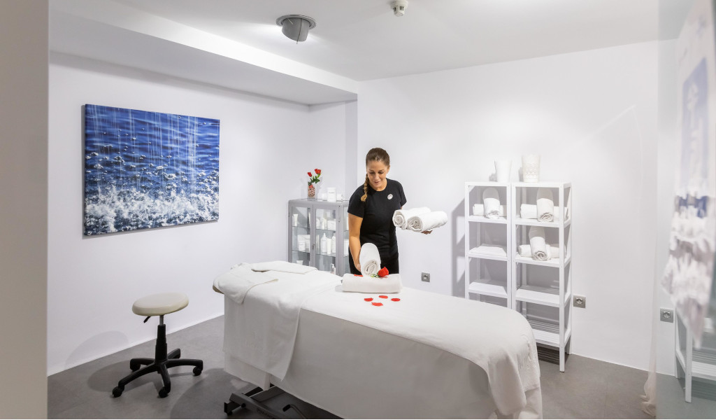 Sala de masajes con terapeuta organizando toallas blancas en Tenerife.