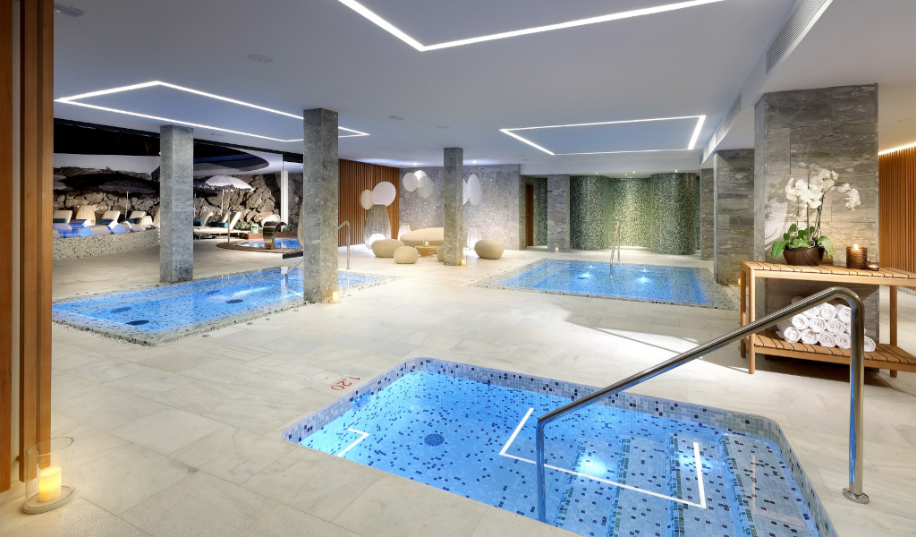 Piscina interior con jacuzzi en un spa de Tenerife, rodeada de plantas y lámparas.
