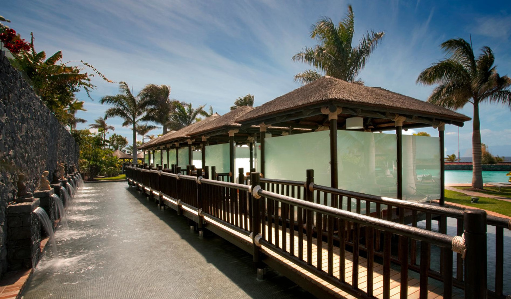 Pasarela de madera con palmeras y muros en Hotel Villa Cortés Tenerife.