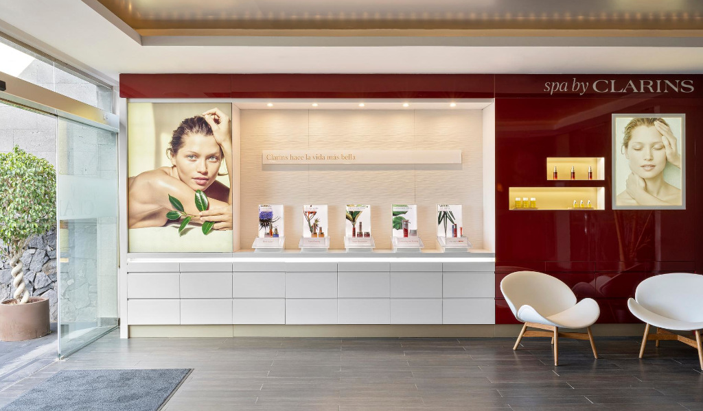 Recepción del spa Clarins en Tenerife con carteles de modelos y productos. Texto: Clarins hace la vida más bella.