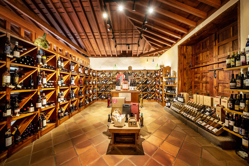 Bodega en Tenerife con estantes llenos de botellas de vino y techo de madera.