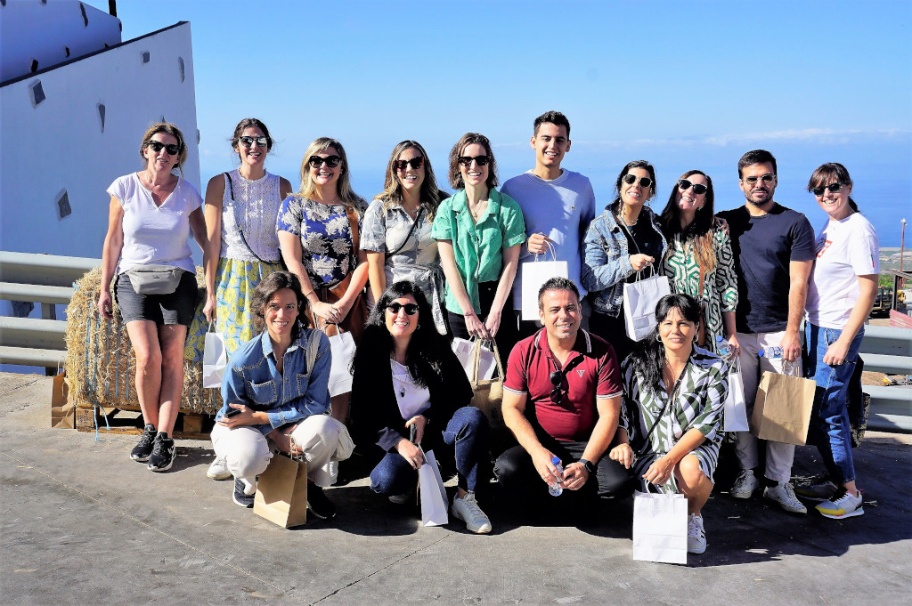 Grupo de personas sonrientes frente al mar en un lugar en Tenerife, con bolsas de regalo.