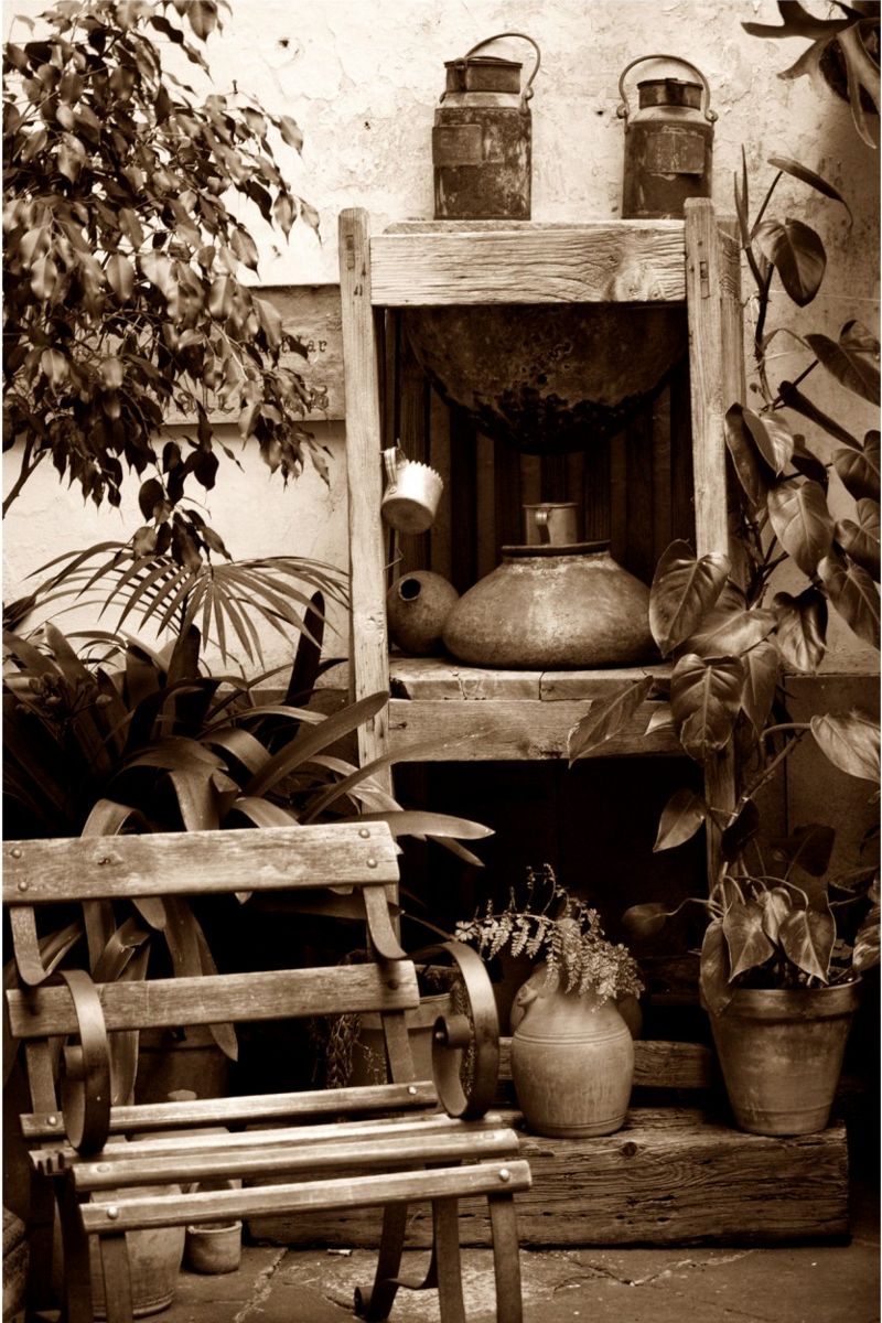 Banco de madera rodeado de plantas y objetos de metal en un patio rústico de Tenerife.