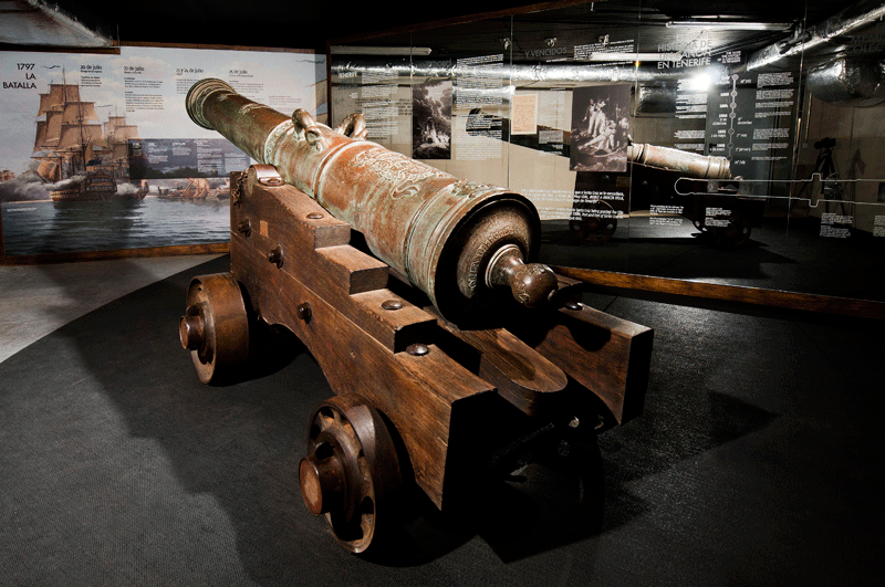 Cañón antiguo en exhibición en un museo de Tenerife, con paneles informativos detrás.