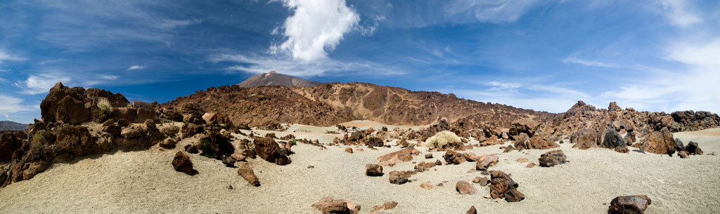 Paisaje volcánico del Teide en Tenerife bajo un cielo azul con nubes dispersas.