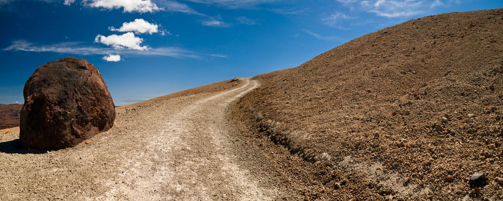 Sendero con roca grande en paisaje árido y cielo azul en Tenerife.