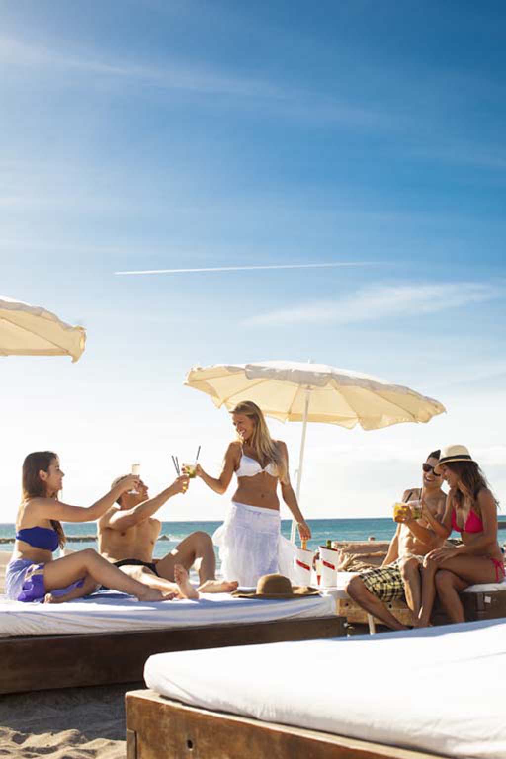 Grupo de personas disfrutando bebidas en la playa en Tenerife bajo sombrillas.