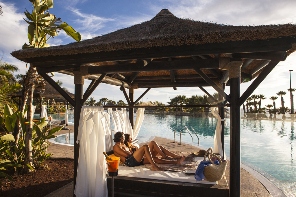 Pareja descansando en una cama balinesa junto a una piscina en Tenerife.