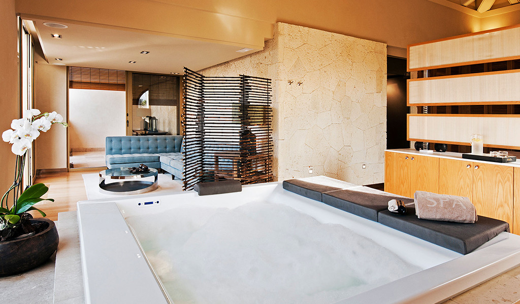 Jacuzzi en sala de spa con sofá azul y orquídea blanca en Tenerife.