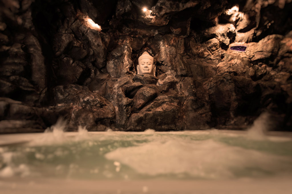 Busto de Buda en cueva rocosa con agua en la base en Tenerife.