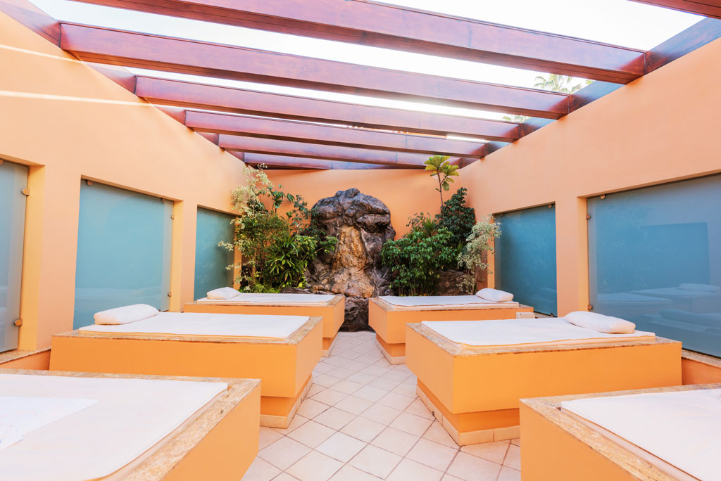 Camas de spa en un salón interior en Tenerife, rodeadas de plantas y luz natural.