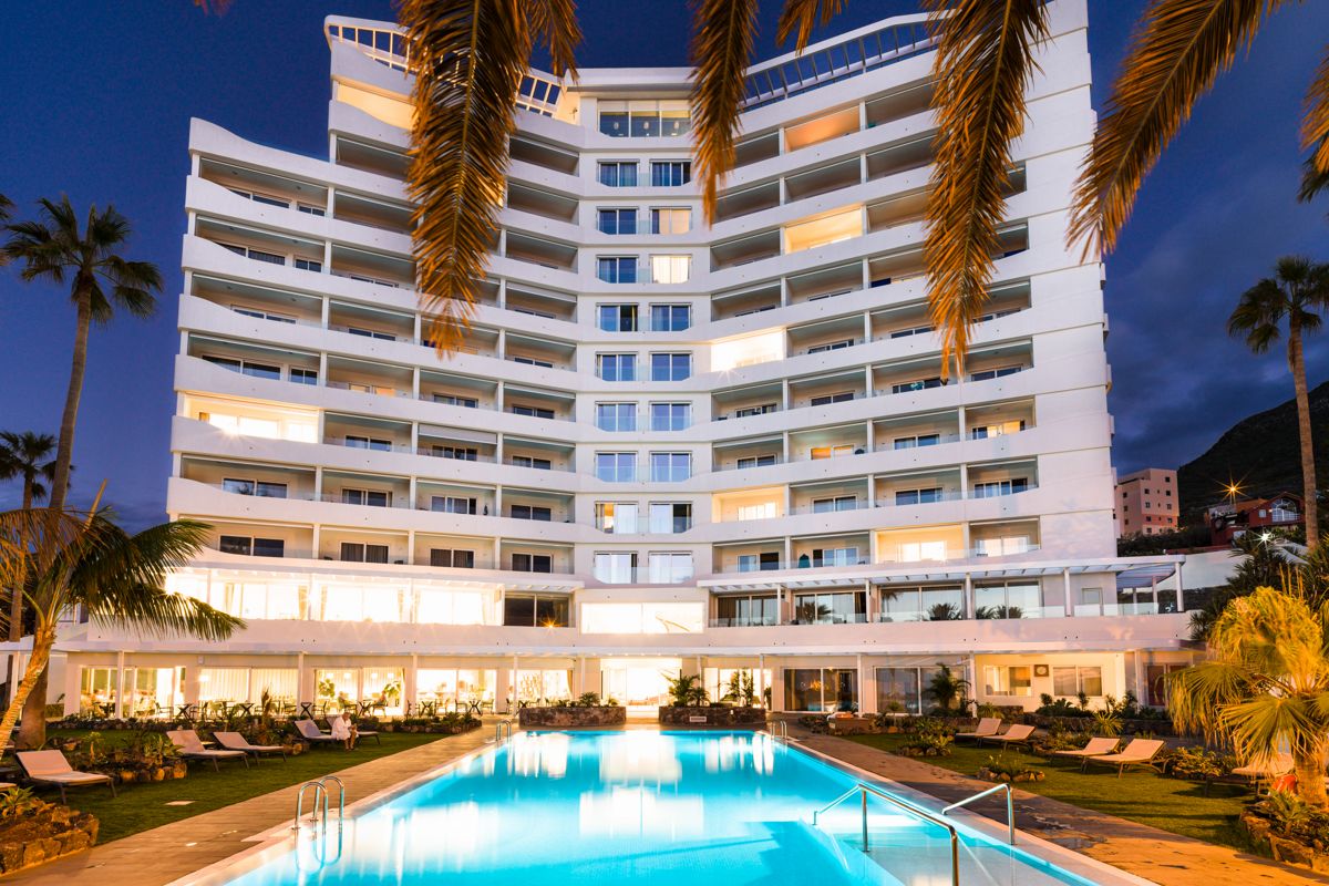 Edificio con piscina iluminada al anochecer en Tenerife, rodeado de palmeras.