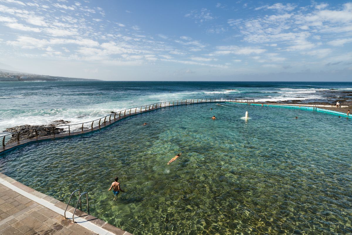 Piscina natural en Tenerife junto al océano con varias personas nadando.