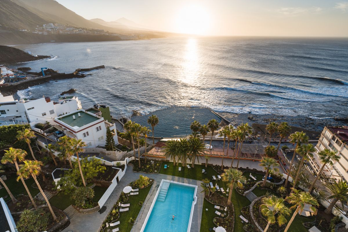 Vista aérea de la costa en Tenerife al atardecer con piscina y jardines.