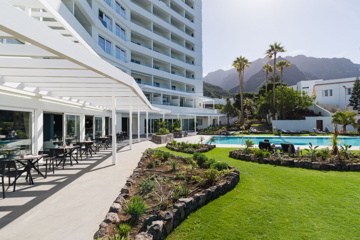 Terraza de un hotel en Tenerife con mesas, piscina y montañas al fondo.