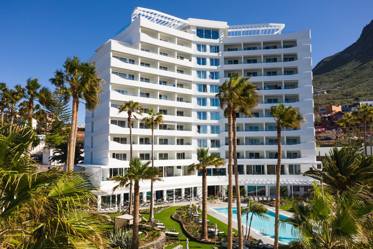 Hotel de varios pisos con palmeras y piscina en Tenerife.
