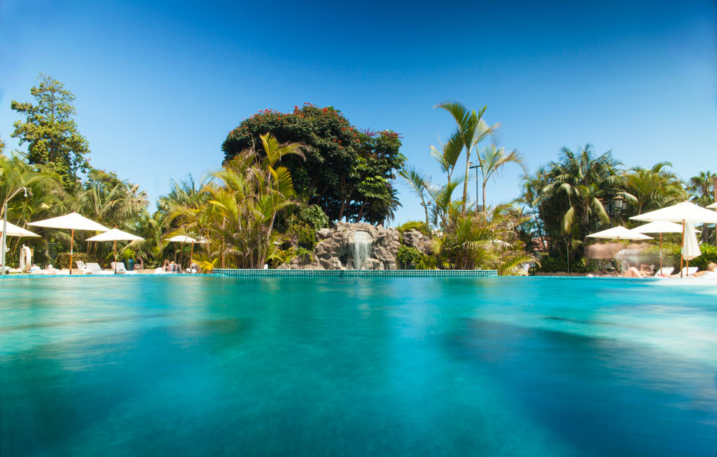 Piscina con sombrillas y vegetación tropical en un hotel de Tenerife.